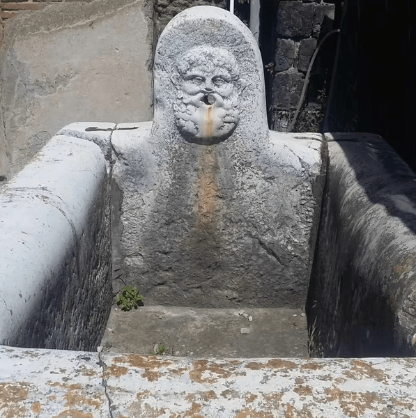 Каменный фонтан в древнем римском городе Геркуланум Древний каменный фонтан с резным лицом в Геркулануме, сохранившийся со времен Римской империи